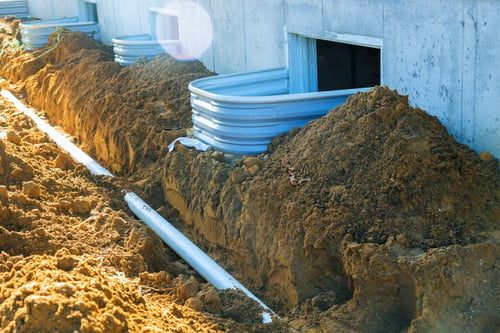 Perimeter drain and window well trench excavated alongside a concrete foundation wall