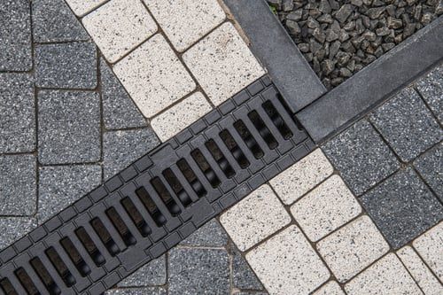 Linear drainage channel installed between paver surfaces to carry surface water away