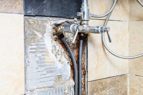 Opened tiled wall exposing pipework during a leak investigation and repair